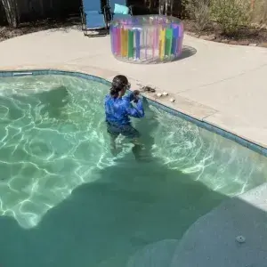 Female pool leak detection technician performing a hands-on inspection in a backyard swimming pool