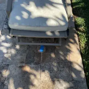 Blue marker flag identifying an underground irrigation or water line leak beneath travertine patio pavers