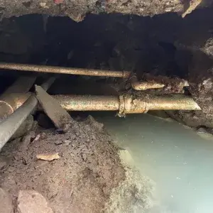 Corroded underground galvanized pipe with active water leak exposed during excavation