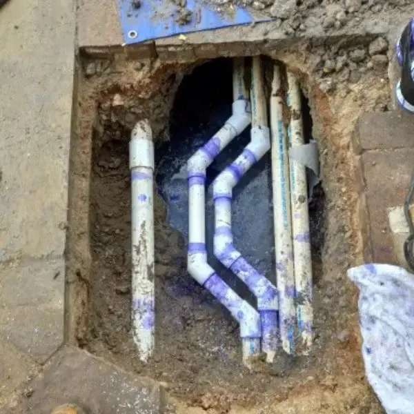 Excavated repair pit exposing rerouted underground PVC plumbing pipes after a slab leak repair